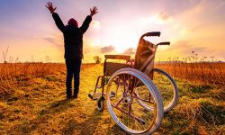 Miracle recovery: young girl gets up from wheelchair and raises hands up. Overjoyed young girl  standing up from a wheelchair outdoors. Shot in meadow. Recovery concept