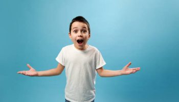 Shocked boy expressing surprise on camera. Facial emotions on blue background with copy space
